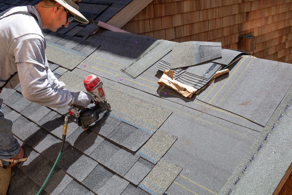 Roofer nailing asphalt shingles on a pitched roof